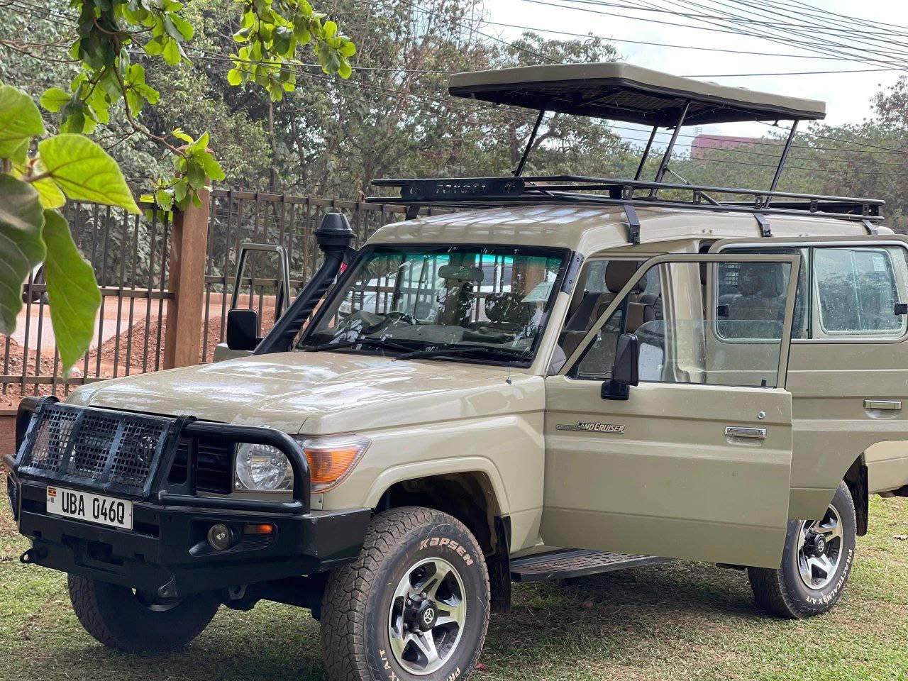 Beige Toyota Land Cruiser with front bumper guard, pop-up roof tent raised, roof rack, and driver's door open.