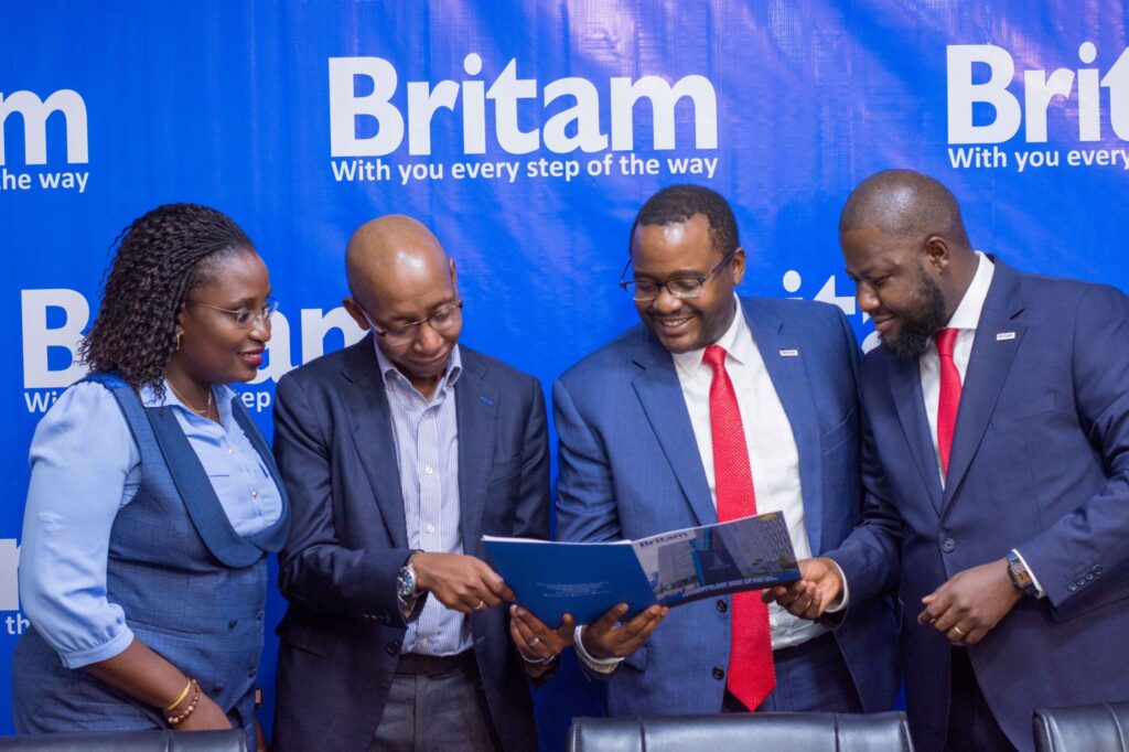 britam-insurance - Rent A Driver Uganda Four professionals in blue suits read a brochure together against a Britam backdrop.
