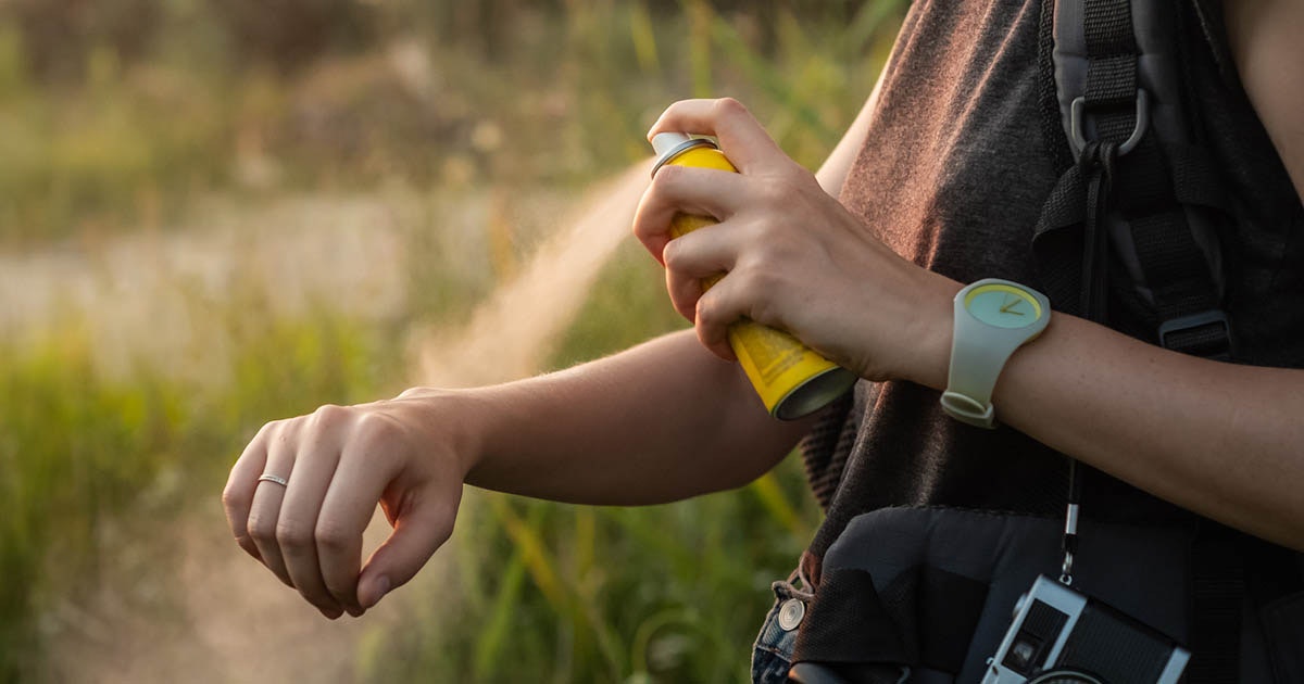 mosquito-repellent-for-travel-in-uganda - Rent A Driver Uganda Person outdoors spraying sunscreen on forearm while hiking.