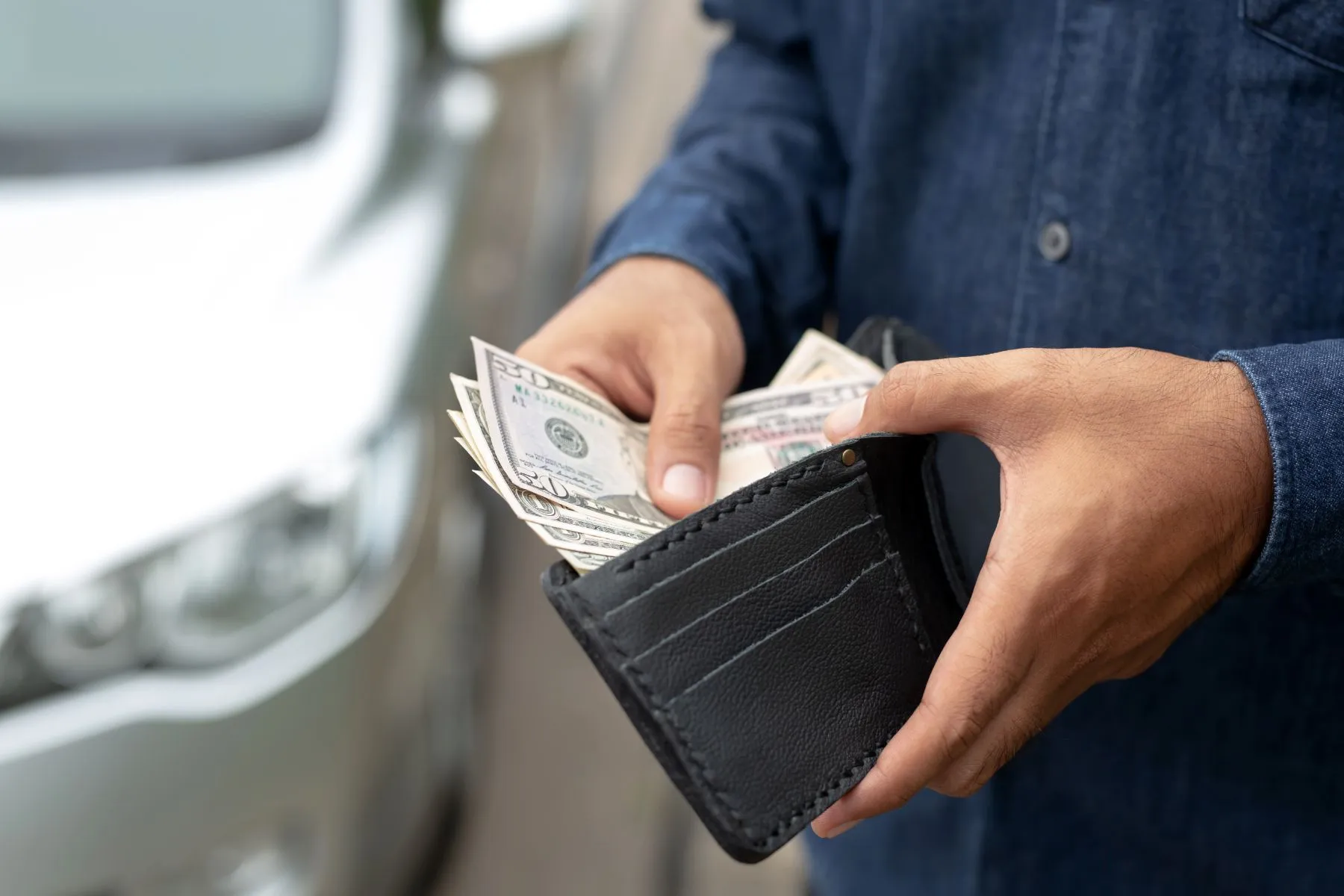 Hands pull cash from a black wallet, showing folded US dollar bills.