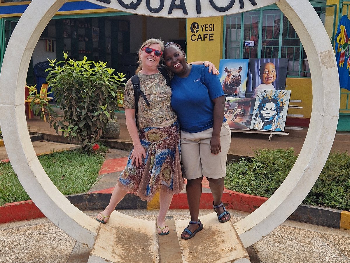 solo-female-travel-uganda - Rent A Driver Uganda Two women posing together inside a large circular sculpture outdoors, with paintings on display in the background.