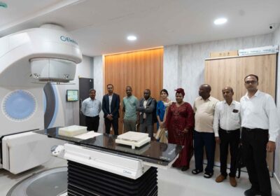Nine People Stand Beside A Large Elekta CT Scanner In A Hospital Imaging Room.